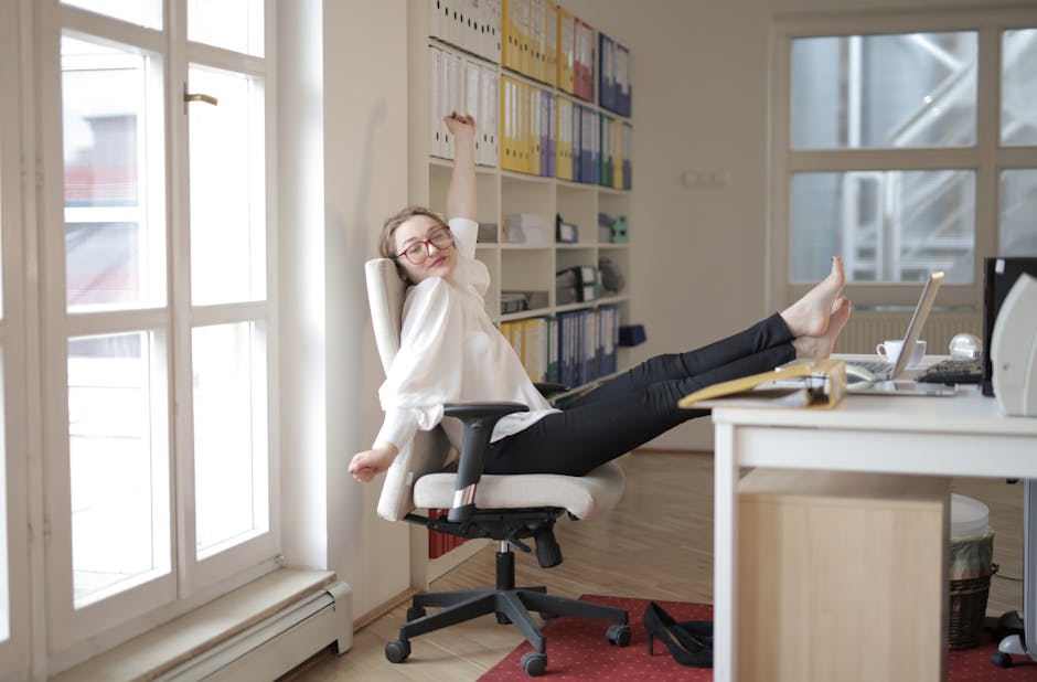 Smiling woman in a bright room taking a short, gentle stretching break near her workspace.